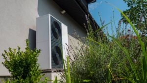 Air to Water Heat Pump unit against the wall outside near bushes