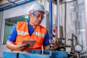 Man in a hard hat and orange vest holding a clipboard inspecting things